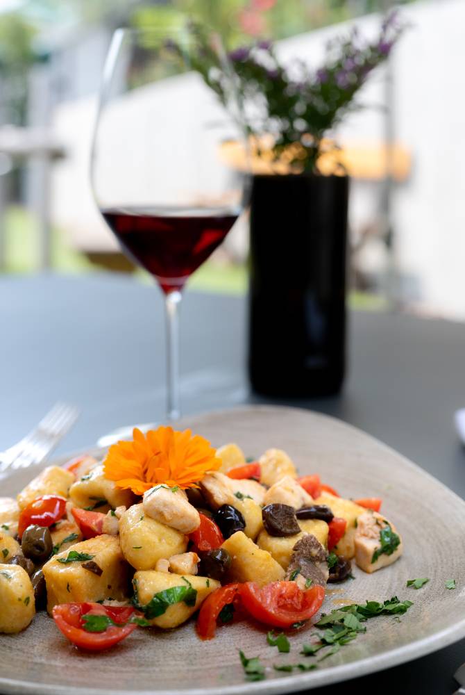 Gnocchi mediterranei con olive, pomodori e un bicchiere di vino rosso Seeperle